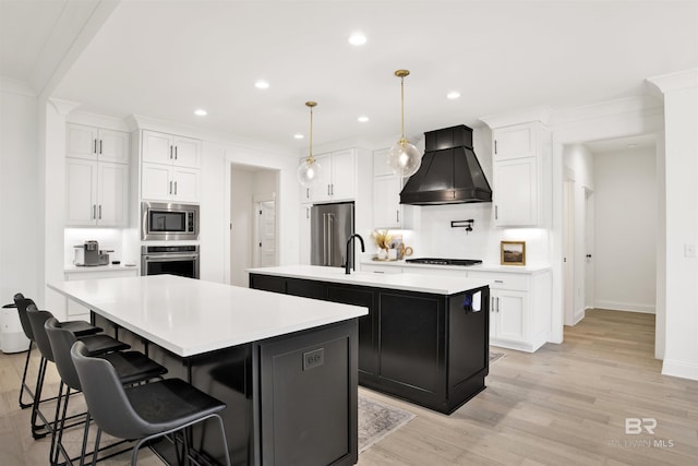 kitchen with white cabinetry, stainless steel appliances, custom range hood, and a center island with sink