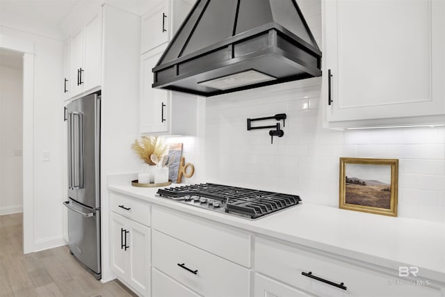 kitchen with tasteful backsplash, light wood-type flooring, appliances with stainless steel finishes, custom range hood, and white cabinets