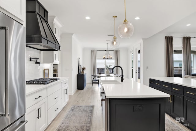 kitchen with appliances with stainless steel finishes, an island with sink, hanging light fixtures, and white cabinets