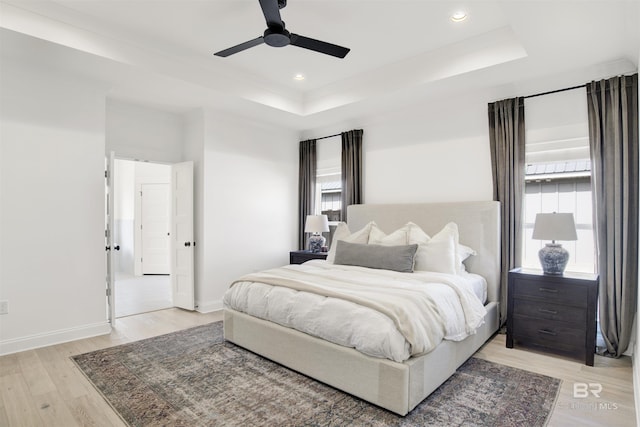 bedroom featuring light hardwood / wood-style flooring, ceiling fan, and a tray ceiling