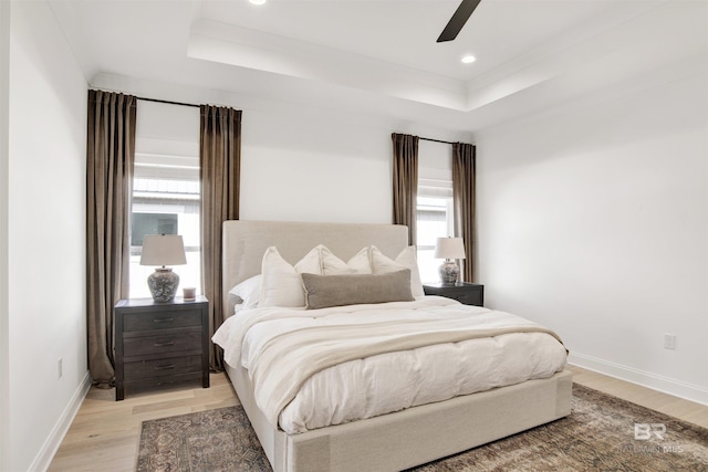 bedroom with multiple windows, a raised ceiling, and light wood-type flooring