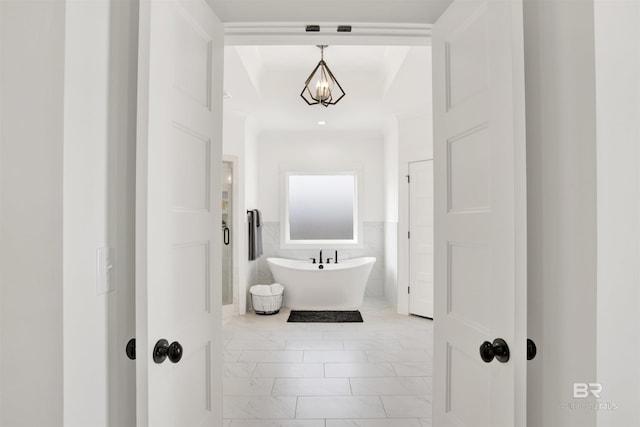 bathroom with tile walls, a bathing tub, and an inviting chandelier