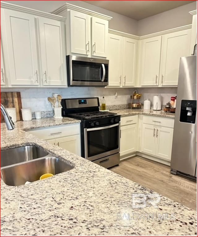 kitchen featuring appliances with stainless steel finishes, light wood-type flooring, white cabinetry, and sink