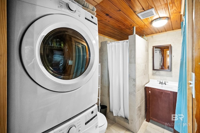 laundry room with sink, stacked washer and dryer, light tile patterned floors, wood ceiling, and tile walls