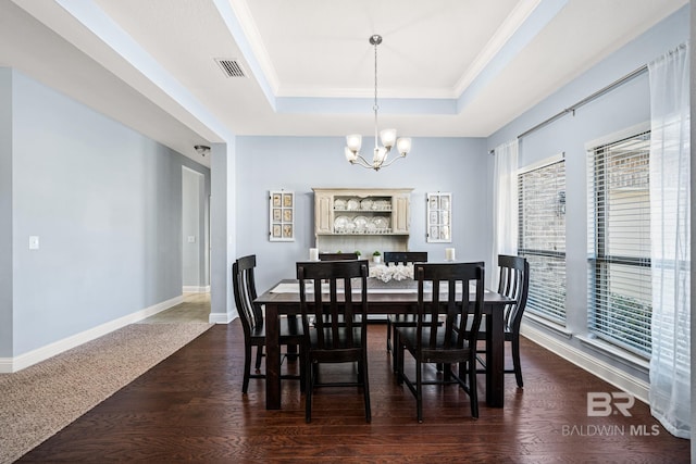 dining area with crown molding, dark wood-type flooring, an inviting chandelier, and a tray ceiling