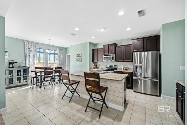 kitchen featuring hanging light fixtures, light stone counters, stainless steel appliances, a notable chandelier, and a kitchen breakfast bar