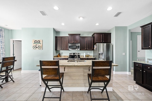 kitchen featuring light tile patterned floors, appliances with stainless steel finishes, light stone counters, sink, and an island with sink