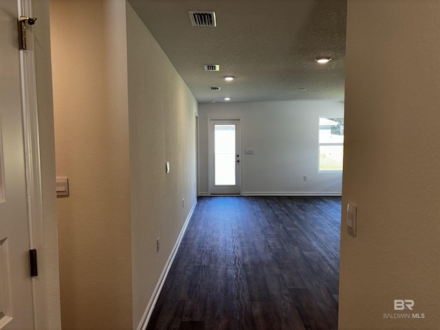 corridor featuring a healthy amount of sunlight, dark hardwood / wood-style flooring, and a textured ceiling