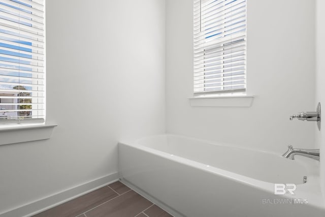 bathroom with wood tiled floor, a bath, and baseboards