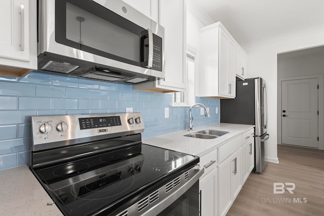 kitchen featuring crown molding, stainless steel appliances, tasteful backsplash, white cabinetry, and a sink