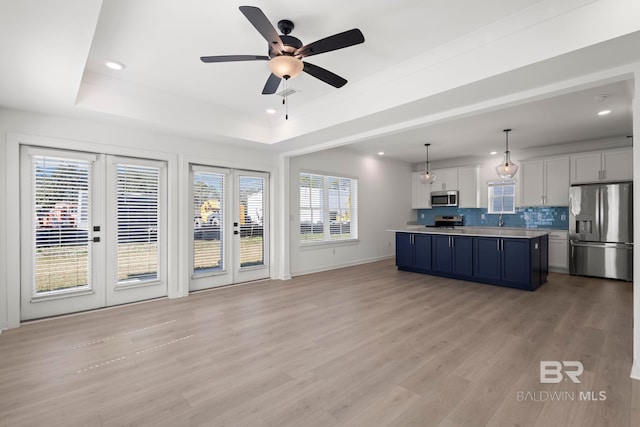 kitchen featuring stainless steel appliances, light wood finished floors, a raised ceiling, and tasteful backsplash