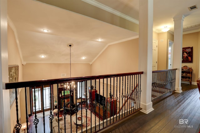 hallway with decorative columns, ornamental molding, vaulted ceiling, dark wood-type flooring, and an inviting chandelier