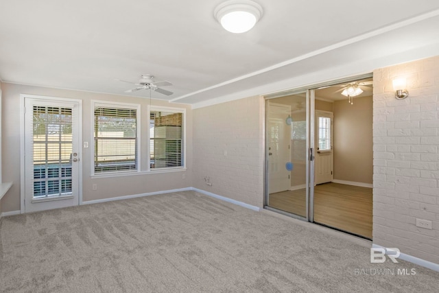 carpeted empty room with ceiling fan and brick wall