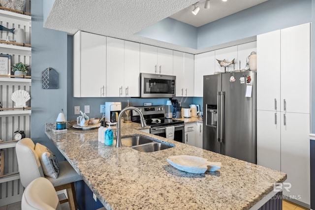 kitchen with a peninsula, a sink, stainless steel appliances, white cabinets, and light stone countertops