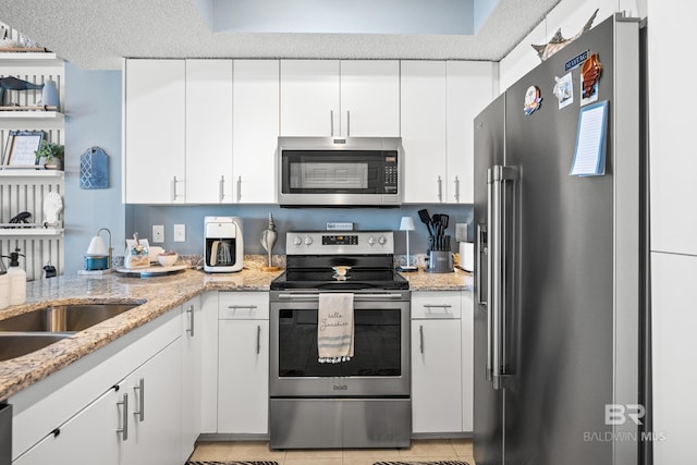 kitchen with a sink, stainless steel appliances, white cabinetry, and light stone counters