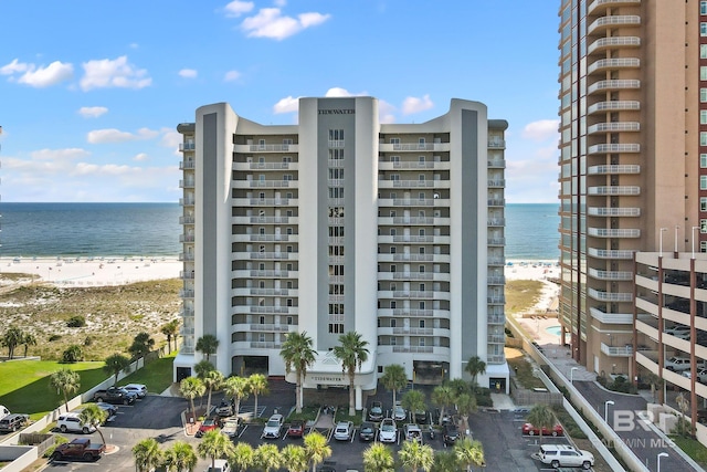 view of building exterior with a water view, a view of the beach, and uncovered parking
