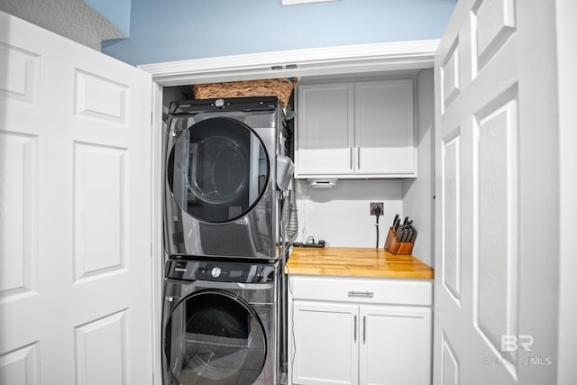 clothes washing area featuring stacked washer / drying machine and cabinet space