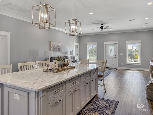 kitchen with hanging light fixtures, ornamental molding, ceiling fan with notable chandelier, a breakfast bar, and a center island