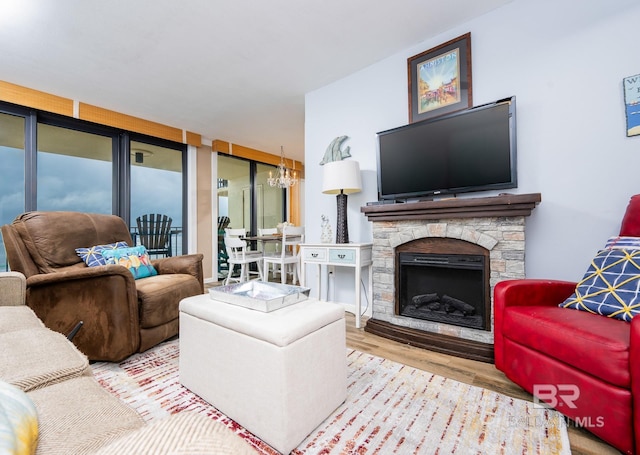 living room featuring a notable chandelier, a stone fireplace, and wood finished floors