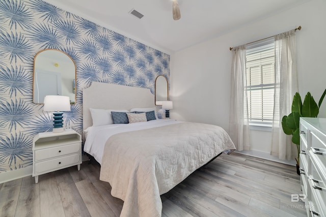 bedroom with light wood-style floors, visible vents, baseboards, and wallpapered walls