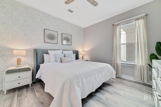 bedroom featuring an accent wall, visible vents, baseboards, light wood-style floors, and wallpapered walls