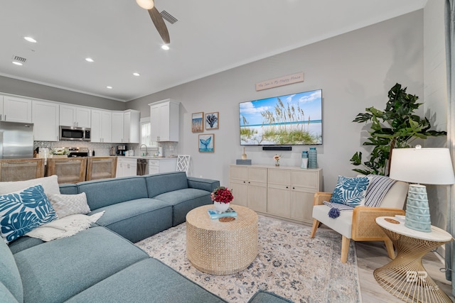 living area featuring a ceiling fan, recessed lighting, visible vents, and ornamental molding