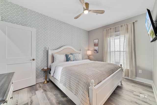 bedroom featuring wallpapered walls, baseboards, ceiling fan, an accent wall, and light wood-style floors