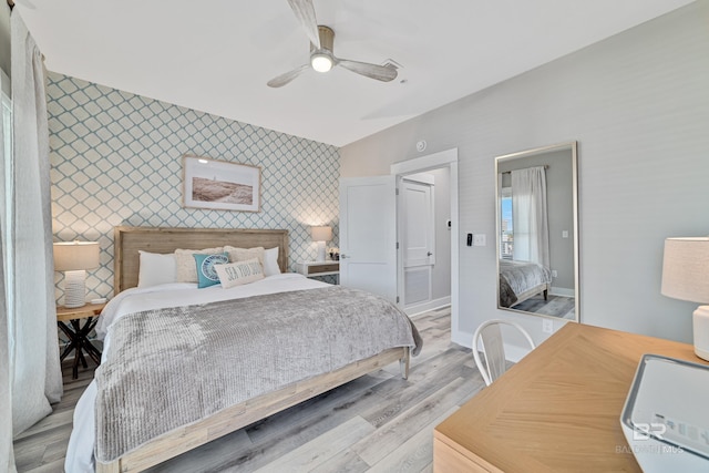 bedroom with light wood finished floors, an accent wall, a ceiling fan, baseboards, and wallpapered walls