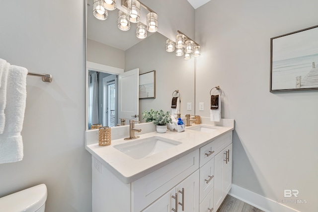 full bathroom featuring double vanity, a sink, toilet, and baseboards