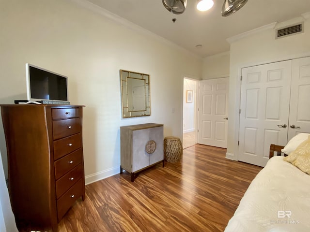 bedroom featuring baseboards, visible vents, wood finished floors, crown molding, and a closet