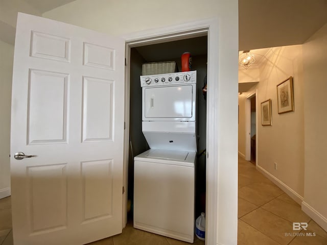 clothes washing area featuring light tile patterned floors, laundry area, stacked washing maching and dryer, and baseboards