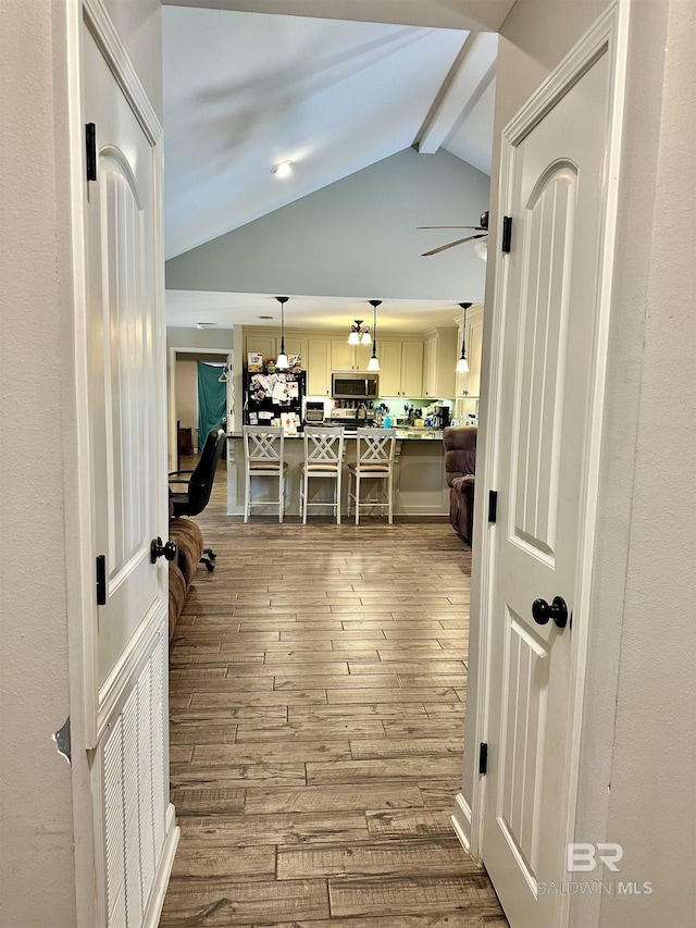 hallway with wood-type flooring and vaulted ceiling with beams