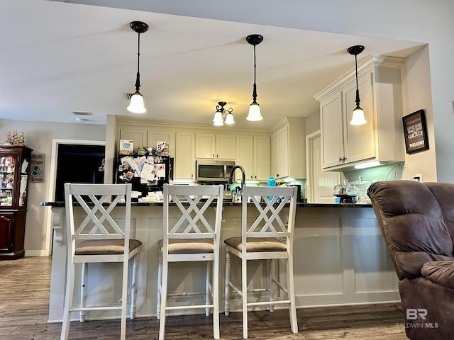 kitchen featuring a breakfast bar area, wood-type flooring, hanging light fixtures, and kitchen peninsula