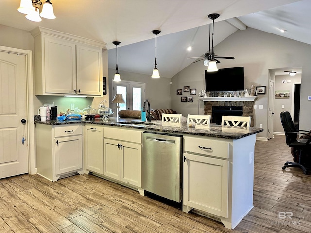 kitchen with sink, light wood-type flooring, a stone fireplace, and stainless steel dishwasher