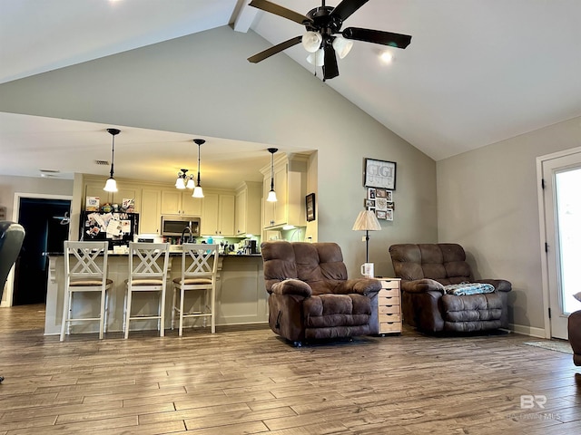 living room featuring ceiling fan, light hardwood / wood-style flooring, and vaulted ceiling with beams