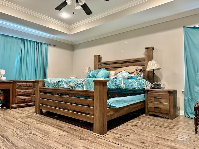 bedroom featuring ornamental molding, light wood-type flooring, ceiling fan, and a tray ceiling