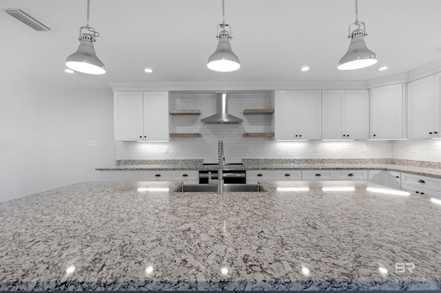 kitchen with hanging light fixtures, wall chimney exhaust hood, and white cabinets