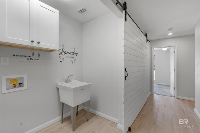 washroom with cabinets, a barn door, hookup for a washing machine, and light wood-type flooring