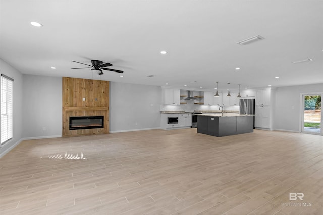 unfurnished living room featuring ceiling fan, sink, a fireplace, and light hardwood / wood-style floors