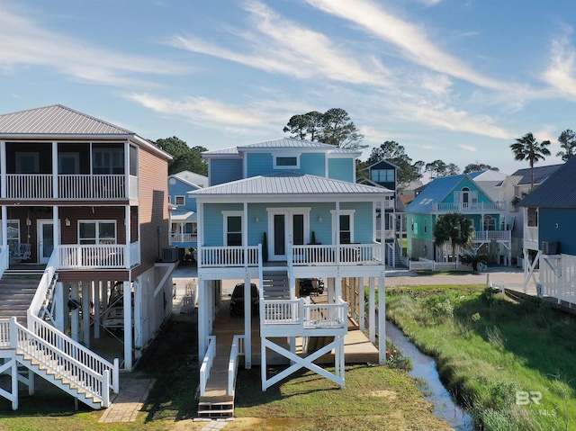 rear view of property with a residential view, stairs, covered porch, cooling unit, and metal roof