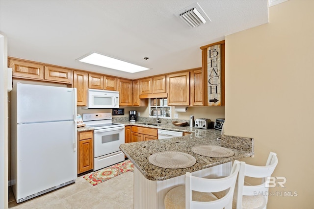 kitchen featuring white appliances, light tile flooring, kitchen peninsula, sink, and a breakfast bar area