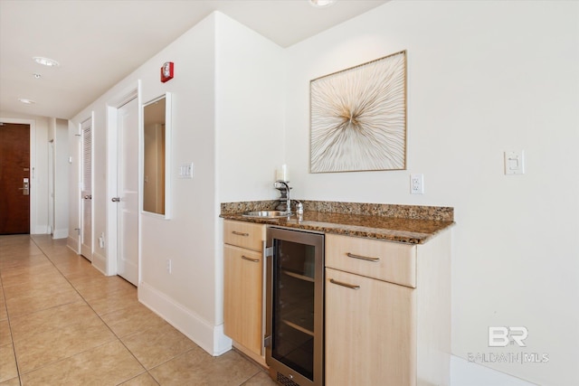 bar featuring dark stone counters, sink, light tile patterned flooring, beverage cooler, and light brown cabinetry