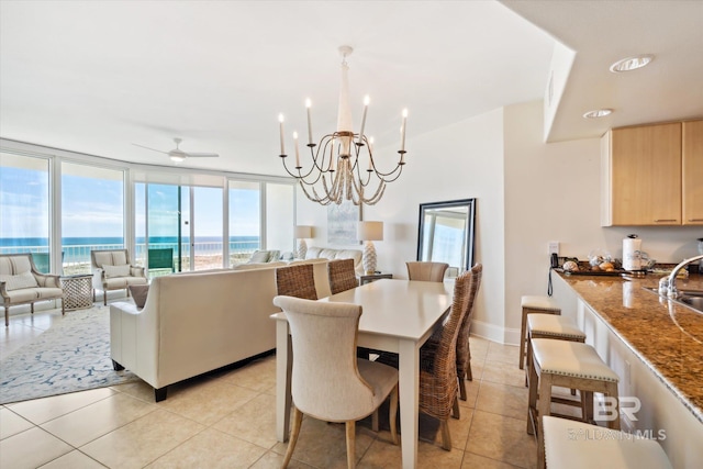 tiled dining space featuring a water view, sink, ceiling fan with notable chandelier, and a wall of windows