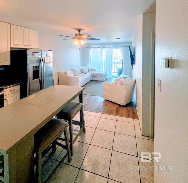 kitchen with stainless steel fridge, a breakfast bar, white cabinetry, ceiling fan, and light wood-type flooring