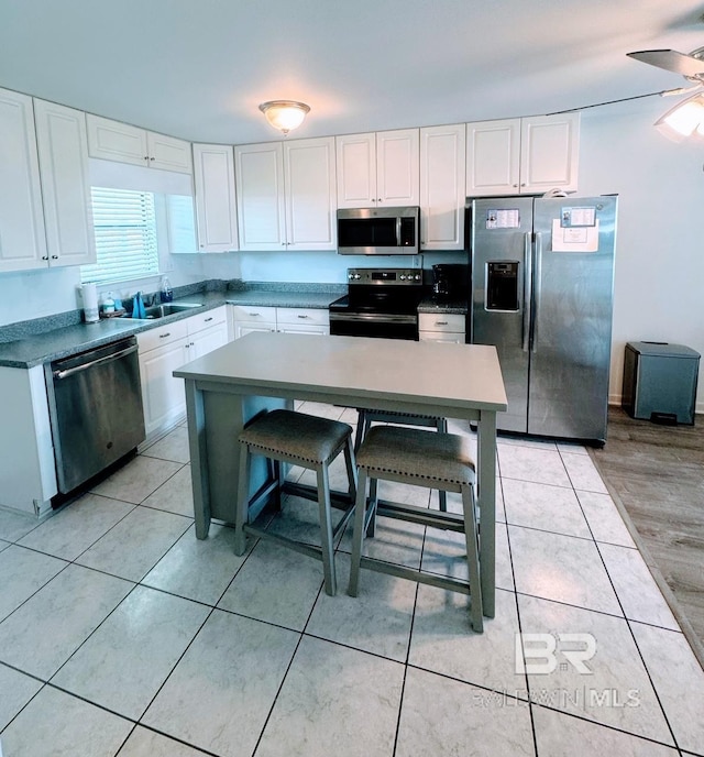 kitchen featuring light hardwood / wood-style flooring, stainless steel appliances, ceiling fan, a breakfast bar, and white cabinets