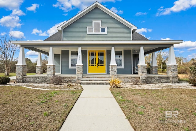 view of front facade featuring covered porch, stone siding, a shingled roof, and a front yard