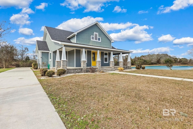 view of front of house featuring a water view, stone siding, a front lawn, and covered porch