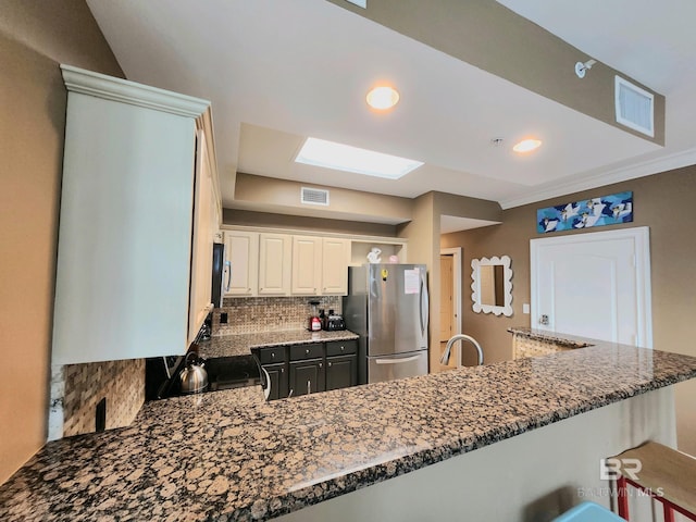 kitchen featuring decorative backsplash, stainless steel fridge, white cabinetry, a kitchen bar, and kitchen peninsula