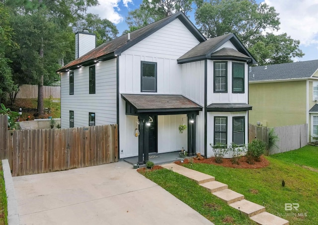 view of front of property with board and batten siding, a front lawn, a chimney, and fence
