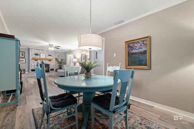 dining space featuring ceiling fan, a fireplace, light hardwood / wood-style flooring, and crown molding